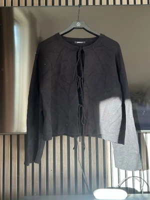 Svart knytkofta från Gina Tricot - Trendig svart kofta från Gina Tricot med knytning framtill. Koftan har rund halsringning, långa ärmar och är tillverkad i mjukt stickat material. Perfekt för lager på lager och enkel att styla till olika outfits.🖤