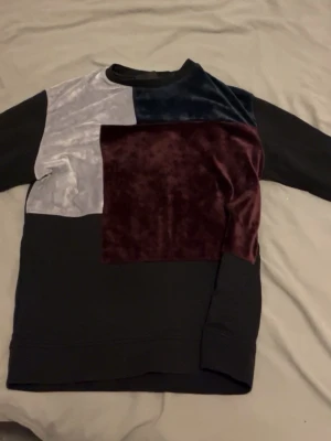 La vichy  - Unik långärmad tröja med patchwork-design i svart, vinröd, mörkblå och ljusgrå sammet samt bomull. Tröjan har rund halsringning och en cool mix av material som ger en trendig look. Perfekt för dig som gillar statement-plagg och vill sticka ut.