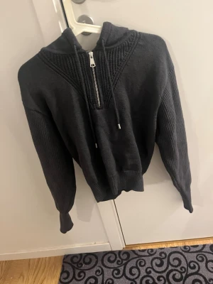 Mörkgrå hoodie med dragkedja - Snygg mörkgrå hoodie med dragkedja framtill och ribbade detaljer på ärmar och axelparti. Tröjan har en stor huva och bred mudd i midjan. Perfekt för en avslappnad och trendig look. Materialet känns mjukt och bekvämt, troligen bomullsblandning.