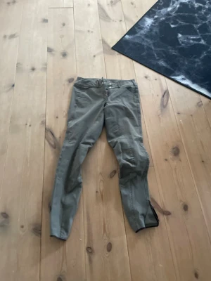 Grå/Gröna Pikeur ridbyxor - Säljer ett par gröna chinos från Pikeur med smal passform och klassisk design. Byxorna har dragkedja och knapp framtill samt detaljer vid benslut. Tillverkade i ett slitstarkt bomullsmaterial som ger både komfort och stil. Nypriset på dessa går runt 2699kr och är väldigt sparsamt använda. Max använda 5 gånger. 