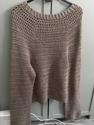 Beige/brun virkad stickad tröja - Säljer en beige/brun, handvirkad stickad tröja med bred halsringning och långa vida ärmar. Tröjan har ett grovt virkat mönster och är gjord i ett mjukt garn, perfekt för lager på lager under kyliga dagar. Står inte storlek men skulle uppskattas som S