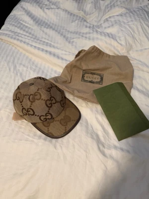 Beige GG Supreme keps från Gucci - Säljer en beige keps från Gucci med det klassiska GG Supreme-mönstret i brunt. Kepsen har böjd skärm, justerbart band i läder baktill och detaljer i canvas. Kommer med dustbag