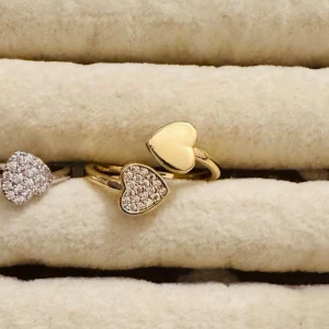 Guldfärgad ring med hjärtan - Trendig guldfärgad ring med öppen design och två hjärtformade detaljer. Ena hjärtat är slätt medan det andra är dekorerat med små glittrande stenar för extra bling. Perfekt accessoar för att lyfta din stil.