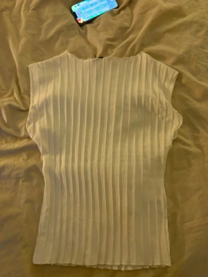 Vit ribbad ärmlös topp - Säljer en stilren vit topp med ribbad struktur och ärmlös design. Toppen har en rak passform och är perfekt att matcha med både jeans och kjol. Enkel men ändå trendig look!