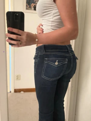 Mörkblå bootcut jeans  - Säljer ett par mörkblå bootcut jeans med vita kontrastsömmar och snygga fickdetaljer med knapp bak. Jeansen har låg midja. Storlek 158 men passar mig perfekt som är 160 cm lång och har vanligtvis 32/34 i storlek 