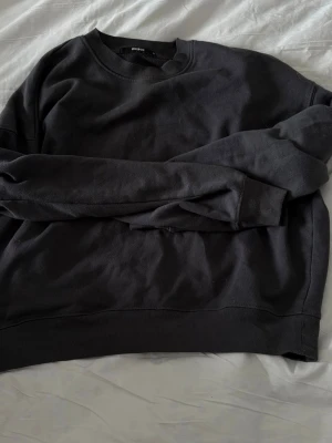 Svart sweatshirt från BikBok - En basic svart sweatshirt från BikBok i storlek M. Tröjan har rund halsringning, långa ärmar och är gjord i mjukt bomullsmaterial. Perfekt för en chill och avslappnad stil. Enkel design utan tryck eller detaljer.