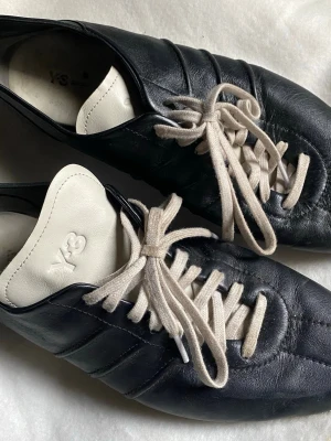 Svarta Y-3 loafers i läder - Säljer ett par svarta loafers från Y-3 med vit plös och vita skosnören. Skorna är tillverkade i mjukt läder och har en signaturdetalj på sidan. Snygg retroinspirerad design som sticker ut med kontrastfärger och subtil branding.