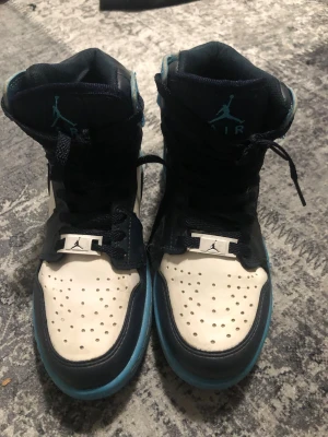 Jordan 1 High blå och vita sneakers - Först till kvarn den. Snygga Air Jordan 1 High sneakers i blått, vitt och svart. Skorna har klassisk hög siluett, perforerad tåbox och ikoniska Jumpman-loggor på plös och häl. Tillverkade i läder med kontrasterande detaljer och svart snörning. Perfekta för dig som gillar streetwear och basketstil.