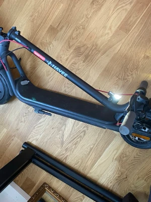 Svart elscooter från NAVEE - Säljer en svart elscooter från NAVEE med digital display på styret. Scootern har röda detaljer på kablarna och robust ram i metall. Perfekt för att ta sig fram snabbt i stan och smidig att fälla ihop när den inte används.