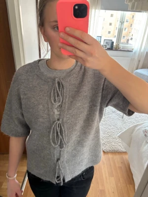 Grå stickad tröja med knyt framtill - Grå stickad kortärmad kofta från Gina tricot. Man kan knyta upp rosetterna. Wool blend. 