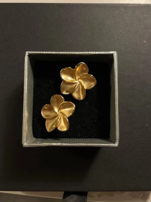 Guldiga blomörhängen  - Snygga örhängen i form av blommor med fem blad, i en matt guldig färg. De har en stilren och trendig design som verkligen sticker ut. Köpte utomlands och har aldrig använt.