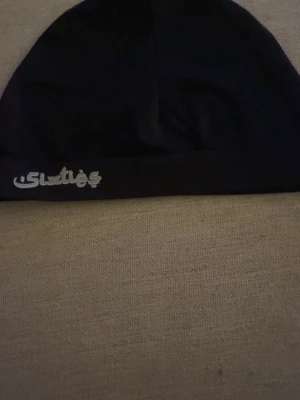 Svart mössa från Sixties - OG OG OG OG OG OG OG  stilren svart mössa från Sixties med diskret logga i silver på kanten. Mössan har en klassisk form och är tillverkad i mjukt syntetmaterial som sitter skönt på huvudet. Perfekt för dig som gillar enkel och clean stil. 