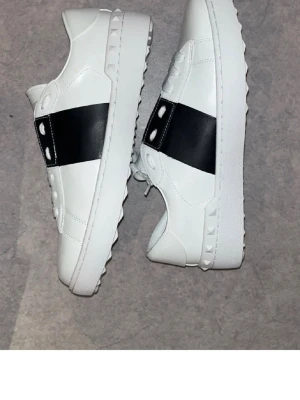 Valentino Garavani vita sneakers - Snygga vita sneakers från Valentino Garavani med bred svart rem över sidan.  Priset är absolut inte hugget i sten