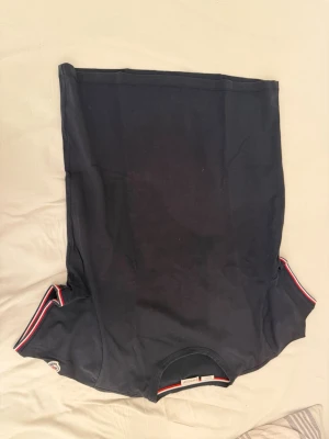 Svart Moncler t-shirt med logga - Snygg svart t-shirt från Moncler med klassisk logga på ärmen och coola rödvita ränder vid ärmsluten. Perfekt till jeans eller shorts för en clean och stilren look. Gjord i mjuk bomull och har normal passform.