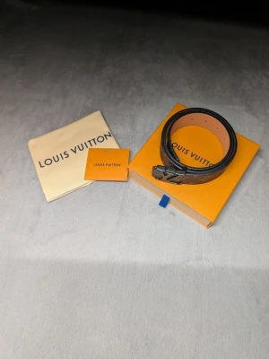 Svart Louis Vuitton monogram bälte - Säljer ett svart bälte från Louis Vuitton med klassiskt monogrammönster och LV-logga i metall på spännet. Bältet har en stilren design och är gjort i skinn med ljus insida. Perfekt accessoar för att lyfta din outfit. Inkluder dustbag och original box med mera! Priset är inte sten, budar med seriösa priser.