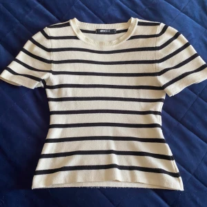 Randig croppad topp från Gina Tricot - Säljer en croppad topp från Gina Tricot i beige med svarta horisontella ränder. T-shirten har rund halsringning, korta ärmar och är stickad i ett mjukt material. Perfekt för dig som gillar en enkel men trendig look. Däremot har tröjan några små fläckar på backsippan av ena axeln men annars är den i topp skick💗