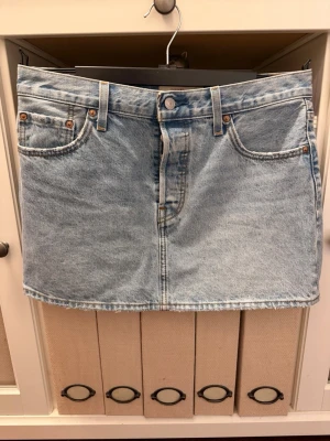 Ljusblå jeanskjol från Levi's - Snygg ljusblå jeanskjol från Levi's med klassisk femficksdesign och bälteshällor. Kjolen har en rak, kort passform och är gjord i slitstark bomull. Perfekt till vardags för en avslappnad och trendig look.