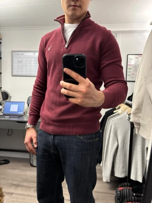 Vinröd halvzip tröja från Gant - Snygg vinröd tröja från Gant med halv dragkedja och broderad logga på bröstet. Tröjan har ribbade muddar vid ärmslut och nederkant samt en klassisk ståkrage. Perfekt till jeans för en clean och stilren look.