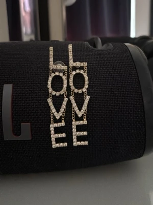 Guldiga LOVE örhängen med stenar - Säljer dom här örhängena för dom aldrig kom till andvndning och dom är köpta i italien köpte dem för 300kr och har använt dom en gång bara så dem e som helt nya💞