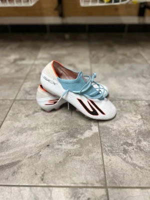 Sketchers fotbollsskor - Säljer ett stilrena skechers fotbollsskor i vitt med ljusblå snörning och detaljer i svart och orange. Skorna har en låg profil, syntetiskt material och dobbar för spel på gräs. Perfekta för dig som vill ha snabbhet och kontroll på planen. Storlek 40,5 men passar från 40-42 då sketchers är större i storlekarna. Använda ett fåtal gånger. Nypris runt 2600, Priset går att diskutera!