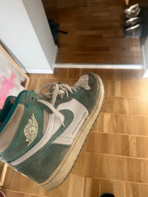 Air Jordan 1 Retro High Turbo Green - Säljer ett par Air Jordan 1 Retro High Turbo Green med vit och turkos mocka och läder. Klassisk vinge-logga på sidan och Nike Swoosh i vitt. Högt skaft och perforerad tåbox för extra ventilation. Skön och ikonisk sneaker för dig som gillar streetwear.