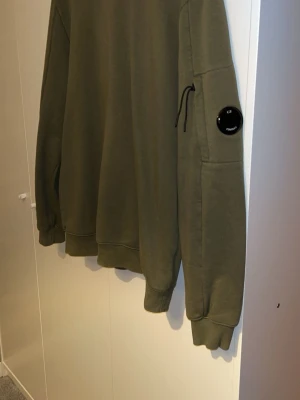 Olivgrön sweatshirt från C.P. Company - Säljer en olivgrön sweatshirt från C.P. Company som knappt är använd, eftersom jag vuxit ifrån den. Inga skador noppor eller fläckar skicket är helt perfekt. Kom dm för mer bilder 