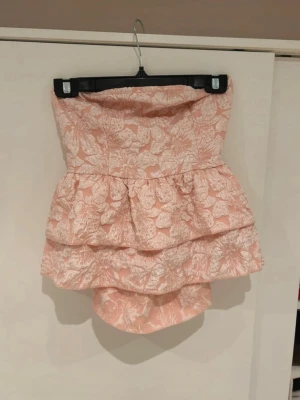 Rosa volangtopp med rosett - Supersöt topp i ljusrosa med vitt blommönster, rosett i ryggen & volanger. Använd 1 gång 