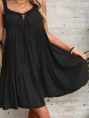 Svart kort klänning med volang - Säljer en svart, luftig kortklänning med volangdetaljer och smala axelband. Klänningen har en söt knytning framtill och är tillverkad i ett mjukt bomullsliknande material. Perfekt för varma dagar och enkel att styla med smycken.