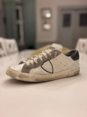 Vita och grå Philippe models med mockadetaljer - Ett par Philippe models i bra skick, de är andvända men inget som syns utanpå eller påverkar andvändningen. Enda som är dåligt är innersidan har gått sönder lite men  inget som syns vid andvändning eller påbvärkar på något sätt. Inget tillbehör medföljer därav pris… tveka inte på att höra av dig vid minsta lilla intresse!