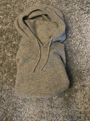 Grå Kashmir hoodie med huva - Mysig grå Kashmir hoodie med huva och dragsko. Långärmad modell med ribbade muddar vid ärmslut och nederkant. Perfekt för en avslappnad och stilren look. Materialet känns mjukt och skönt mot huden.