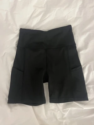 Svarta cykelshorts med fickor - Snygga svarta cykelshorts med hög midja och praktiska sidofickor. Tillverkade i stretchigt material som passar perfekt för träning eller en aktiv vardag. Klassisk och enkel design utan synliga loggor.