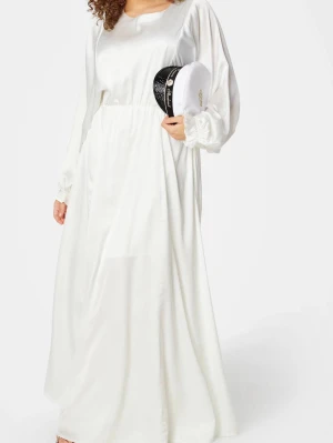 Vit långklänning med långa ärmar - Elegant vit långklänning med rund halsringning och långa, lösa ärmar med resår vid handlederna. Klänningen har en mjuk, flytande passform och markerad midja för en smickrande siluett. Perfekt för dig som gillar stilrena och klassiska looks.