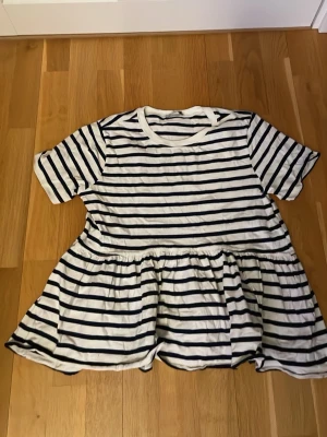 Randig topp med volang från Zara - Supersöt topp från Zara i vitt och marinblått med horisontella ränder. Modellen har korta ärmar, rund halsringning och en volang nedtill som ger en avslappnad och trendig look. Perfekt till jeans eller kjol för en fräsch stil.