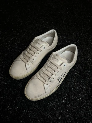 Saint Laurent sneakers - Snygga sneakers från Saint Laurent med handskriven logga på sidan. Relativt bra skick, finns tecken på användning, som att sulan har släppt lite på sidan på vissa ställen och lite små missfärgningar här och där (syns inte om man gör en noggrann inspektion). Överlag fint skick, är bara ärlig med kunderna och nämner allt som kan anses som användning. Inget tillbehör medföljer.