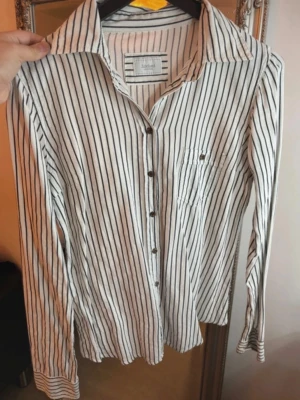 Randig skjorta från Subdued - Vit skjorta med svarta vertikala ränder från Subdued. Klassisk krage, knäppning framtill och en bröstficka. 