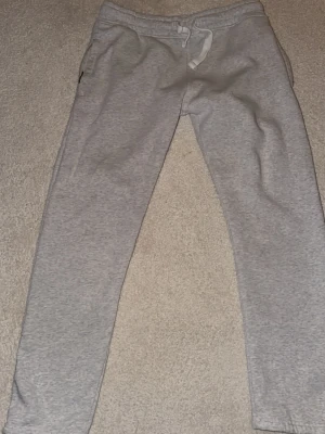 Ljusgrå mjukisbyxor från Russemerch - Ljusgrå mjukisbyxor från Russemerch med bekväm resårmidja och vit dragsko. Tillverkade i mjukt bomullsmaterial och har raka ben. Perfekta för chill dagar och enkel stil.