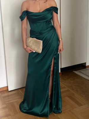 Mörkgrön balklänning  - Säljer min fina mörkgröna balklänning i satin. Den är i storlek 4, motsvarar XS/34. Off-shoulder modell med korsettmidja och slits. Använd endast en gång, som ny. Jag är 160cm och bar klackar, men den passar även lite längre💞 Nypris ca 2000kr.