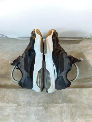 Svarta Nike Air jordan sneakers - Säljer ett par svarta Nike Air jordan sneakers med vit sula och synlig luftbubbla. Skorna har detaljer i mesh och syntet, samt röda accenter vid hälen. Klassisk sportig look med lågt skaft och robust yttersula för bra grepp.