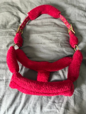 Röd fluffgrimma - Säljer en röd grimma till häst med mjuk, fluffig vaddering och guldfärgade metalldetaljer. Den är justerbar på båda sidor av nackstycket. Hundar finns i hemmet