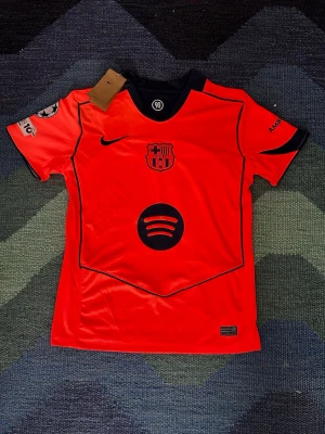 Röd FC Barcelona matchtröja Nike - Säljer en röd FC Barcelona matchtröja från Nike med svarta detaljer och tryck. Tröjan har klubbmärke, Nike-logga och Spotify som sponsor framtill. Korta ärmar med tryck på båda sidor och svart krage. Perfekt för dig som älskar fotboll och Barca! Storlek S och pris på 450 där priset kan diskuteras eftersom att det finns en mindre fläck på baksidan längst ner där man inte märker av den alls.