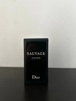 Dior Sauvage Eau de Parfum - Dior Sauvage Eau de Parfum i elegant svart glasflaska med matchande svart kartong. Flaskan har en stilren, rund form och tydlig logga framtill. En ikonisk doft som utstrålar lyx och modernitet, perfekt för dig som gillar exklusiva parfymer.