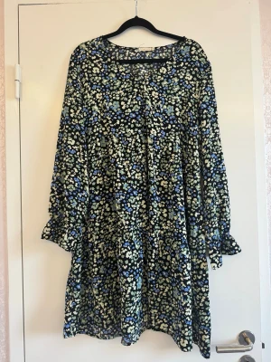 Blommig kortklänning med volang - Söt kortklänning med blått, vitt och grönt blommönster. Klänningen har långärmade ärmar med lätt volang vid ärmslut och en lös, flowy passform. Perfekt för vår och sommar med sin lätta känsla och fina detaljer. Köpt i Frankrike och där har dem mindre storlekar så skulle säga att den sitter mer som en L men funkar bra om du har M i storlek då den också satt perfekt på mig med M i storlek. Endast använd ett fåtal gånger. 