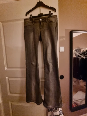 Grå bootcut jeans med slitningar - Säljer ett par grå bootcut jeans med lätt slitna detaljer och klassisk femficksmodell i strl 28/30. De är från weekday.Jeansen har låg midja och utsvängda ben, vilket ger en retro och avslappnad vibe. Perfekta för dig som gillar en tidlös men ändå trendig look.