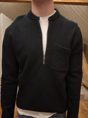 Svart halvzip tröja med bröstficka - Svart långärmad tröja med halvzip och liten bröstficka. Varm och fin. Finns ett litet hål men det syns inte vid användning. Lätt att laga!