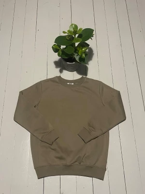 Beige sweatshirt med rund hals - En stilren beige sweatshirt med rund halsringning och långa ärmar. Tröjan har ribbade muddar vid ärmslut och nederkant. Perfekt för en avslappnad och enkel look. Materialet ser ut att vara mjuk bomullsblandning. Storleken på denna tröja är 146/152 men om du är osäker på storleken kolla gärna måtten nedan.                                                           Axelbredden är 40cm och längden är 58cm