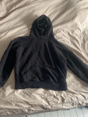 Svart hoodie - En klassisk svart hoodie med huva och dragsko, samt en stor magficka framtill. Hoodien har ribbade muddar vid ärmslut och nederkant. Perfekt för en avslappnad och stilren look.