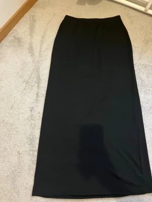 Svart lång tajt kjol  - En enkel och stilren svart lång tajt kjol i mjukt bomullsmaterial. Kjolen har rak passform och är perfekt för dig som gillar minimalistisk stil. Inga synliga detaljer eller mönster, bara klassiskt svart.