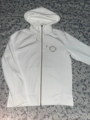 Vit BOSS zip-hoodie – stilren & fräsch - Säljer en vit hoodie från BOSS med dragkedja framtill. Diskret rund BOSS-logga på bröstet. Klassisk modell med huva och justerbara snören samt fickor framtill.  Perfekt både till vardags och för en clean, sportig look.  ✔️ Färg: Vit ✔️ Modell: Zip-hoodie ✔️ Storlek S ✔️ Skick: Mycket fint skick ✔️ Stilren och lättmatchad  Säljes då den inte kommer till användning. Hör av dig vid frågor 😁