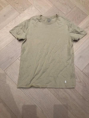 Beige t-shirt från Polo Ralph Lauren - Snygg beige t-shirt från Polo Ralph Lauren med klassisk passform och liten broderad logga i vitt nedtill. Tillverkad i mjuk bomull och har rund halsringning samt korta ärmar. Perfekt basplagg för en clean och enkel stil.