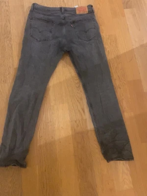 Levis jeans  - Säljer ett par grå Levi's 502 jeans med klassisk femficksdesign och raka ben. Jeansen har en snygg mörkgrå ton och är tillverkade i slitstarkt bomullsmaterial. Passar dig som gillar en enkel och tidlös look med lite smalare snitt.
